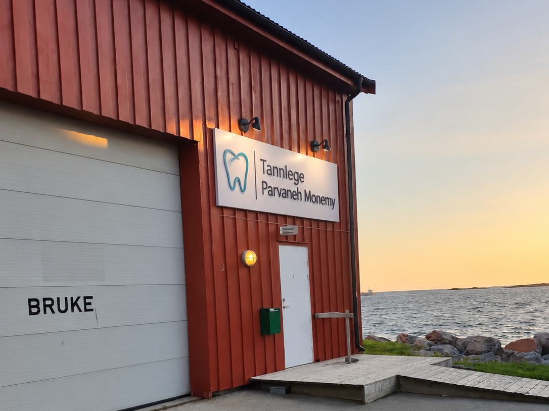 Inngangen til tannklinikken: hvit dør under skiltet «Tannlege Parvaneh Monemy», med sjøen rett utenfor