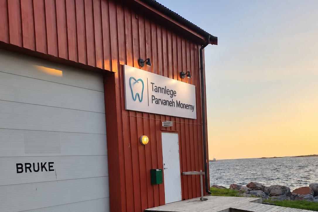 Inngangen til tannklinikken: hvit dør under skiltet «Tannlege Parvaneh Monemy» på det røde bygget, ved siden av garasjeporten
